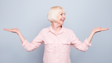 Eine ältere Dame steht im Raum und macht eine sportliche Übung mit den Armen.