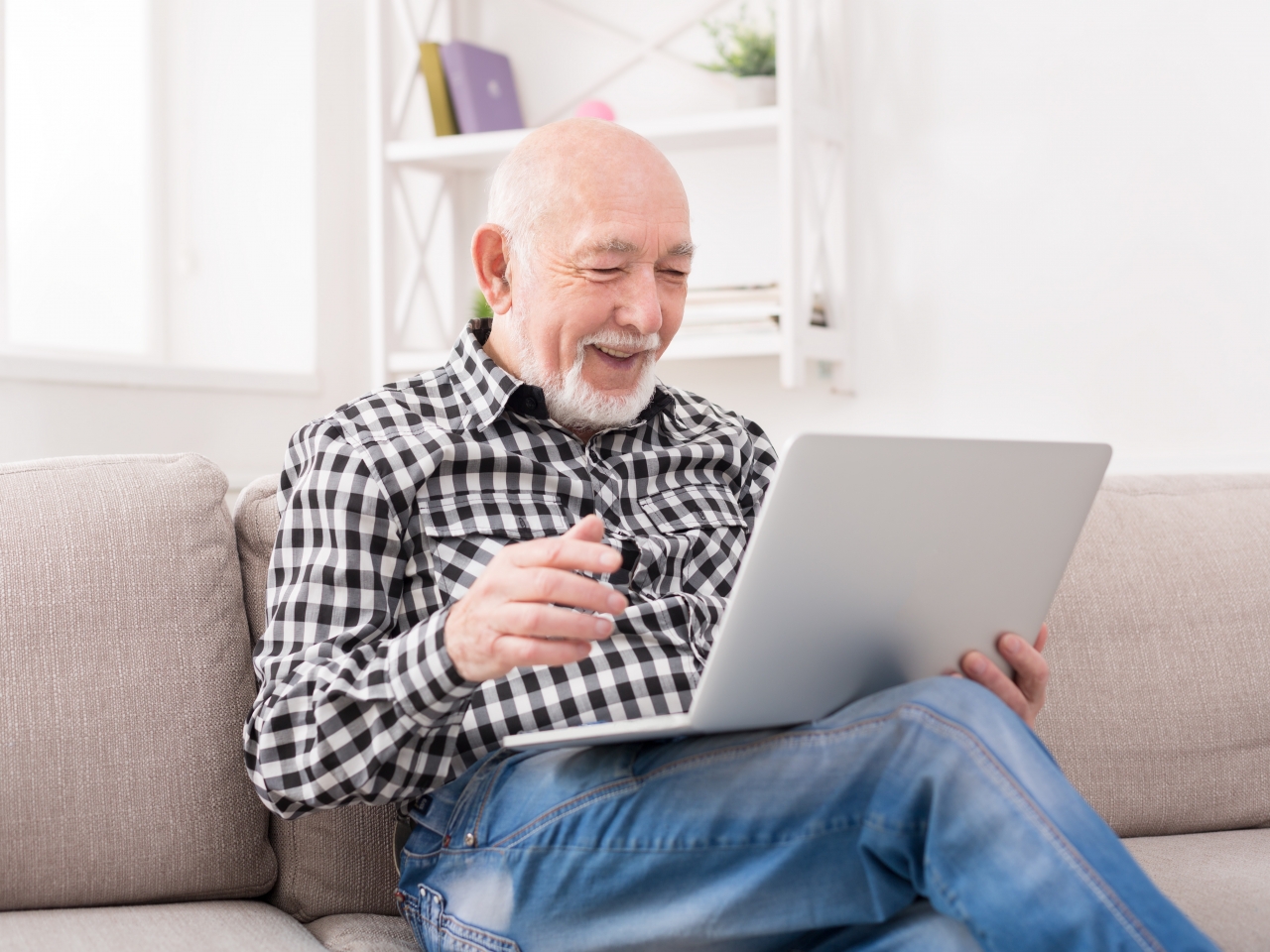 Auf dem Foto sieht man einen Mann, der mit einem Laptop auf dem Schoß auf einem Sofa sitzt