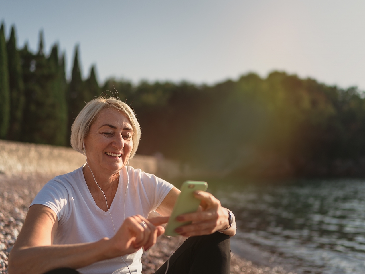 Eine Frau sitzt mit ihrem Smartphone am See